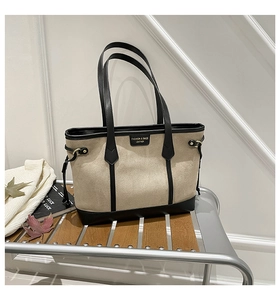 Detail of two-tone tote bag with black leather straps and textured beige fabric