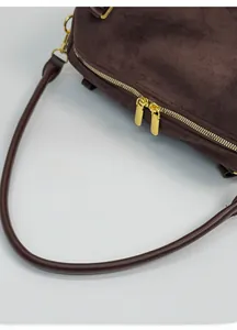 Détail d'un sac en daim marron foncé montrant les coutures et la fermeture éclair dorée