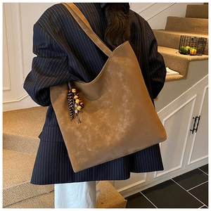 Brown faux suede tote bag with decorative bead charm shown worn by a model on a staircase