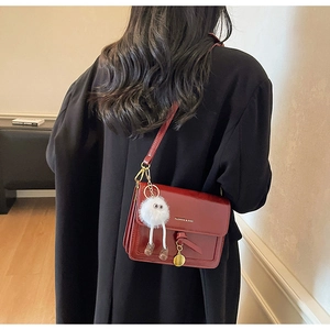 Detail of red leather crossbody bag featuring gold hardware and a cute white plush charm