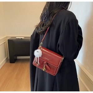 Close-up of deep red rectangular crossbody bag with plush charm on a black coat model