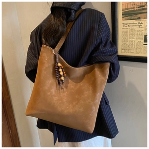 Detailed view of brown suede tote bag featuring a colorful beaded tassel and retro aesthetic