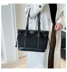 Close-up of black tote bag featuring a metal logo plate and decorative side drawstring detail