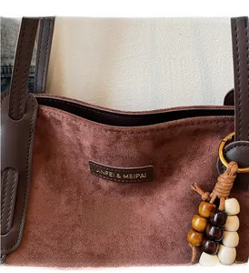 Detail of brown suede tote bag with leather logo tag and decorative wooden beads