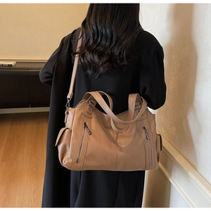 Detail view of large light brown tote bag featuring pebbled texture and functional zip pockets