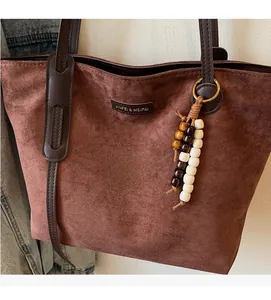 Close-up of brown suede tote bag featuring leather handles and decorative beaded tassel