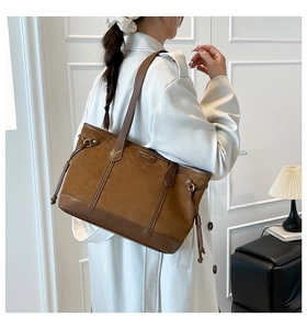 Detail of a brown leather tote bag with side drawstrings and smooth texture on the model