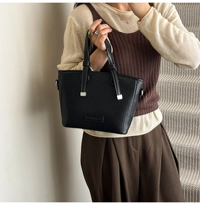 Detail of black woven texture tote bag featuring silver metal accents and dual handles