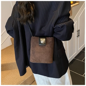 Detail view of brown suede bucket bag with black leather flap and silver metal buckle