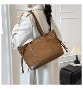 Brown suede tote bag with leather patchwork and drawstring details worn on the shoulder