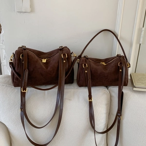 Détail de deux sacs Boston en daim marron foncé de différentes tailles sur un canapé