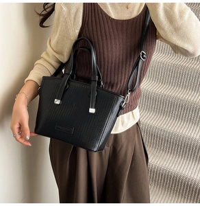 Detailed close-up of a black woven texture tote bag worn as a crossbody on a model