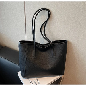 Close-up of black pebble leather tote bag texture resting on an art book in a studio