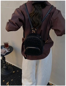 Detail of black mini leopard print backpack with gold hardware worn by model