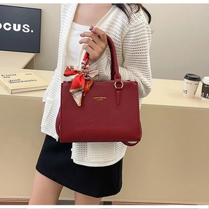 Deep red leather tote bag with silk scarf detail and golden logo held by model