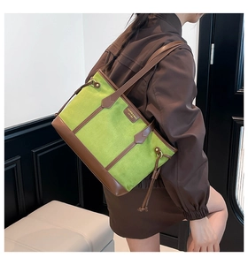 Detail of green suede tote bag featuring brown leather trim and side drawstring accents