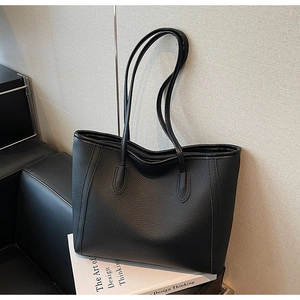 Detailed view of the black pebble leather tote bag resting on a dark chair next to a book