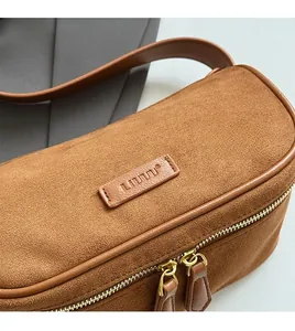 Macro detail of caramel suede texture and leather brand logo on a vintage pillow bag