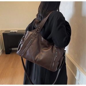 Detail of dark brown lychee leather tote with vintage metal zippers and soft texture