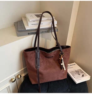 Detail of a large brown suede tote bag with wooden bead pendant and slim leather straps