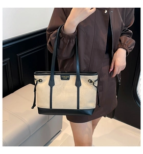 Detail of beige and black contrast tote bag with leather logo patch and thin shoulder strap