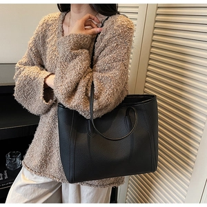 Detail of black pebbled leather tote bag showing textured finish and slim shoulder straps
