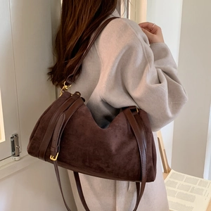Détail du sac à bandoulière en daim marron foncé avec boucles dorées sur manteau gris