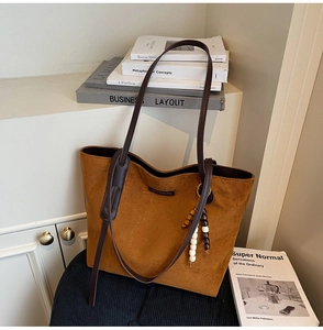 Detail of caramel suede tote bag with dark brown handles and wooden bead charm on a chair