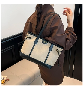 Detail view of beige canvas and black leather tote bag worn on shoulder for commuting
