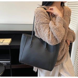 Litchi pattern black leather tote bag shown being worn by a model in a stylish indoor setting
