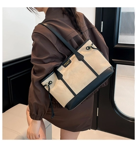 Detailed shot of model wearing a large beige and black patchwork tote bag over the shoulder