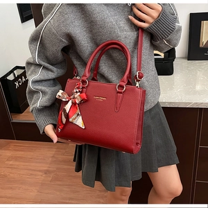 Detail of red lychee leather tote bag with elegant silk scarf wrap and gold logo