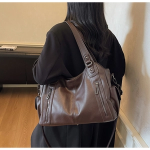 Detailed close-up of dark brown pebble leather tote bag with vintage silver zippers