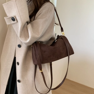 Détail d'un sac cylindrique en daim marron foncé avec texture fine et boucles métalliques dorées