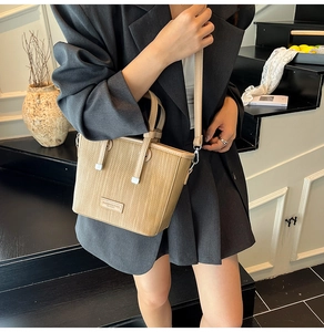 Detail of light khaki woven texture bucket bag with leather strap and fashion label