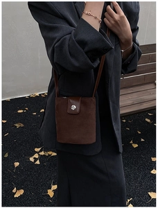 Detail of a brown suede mini crossbody bag featuring a round metallic clasp on the flap