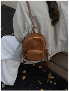 Outdoor shot of a brown suede mini backpack with golden zippers on a girl's back