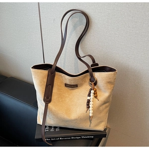 Detail of beige tote bag with dark brown leather handles and wooden bead pendant