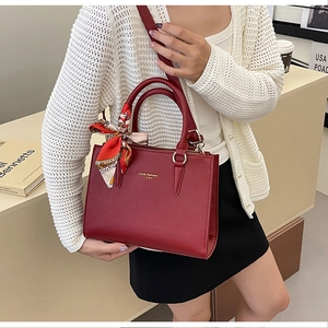 Detail of red leather tote bag with brand logo and decorative patterned silk scarf handle