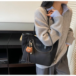 Detail einer großen schwarzen Nylon-Tote-Bag mit Plüschbären-Anhänger an einem Modell