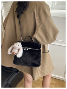 Détail du sac seau en peluche noire avec pendentif lapin brun porté sur un blazer kaki