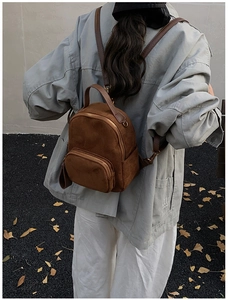 Detail of a brown suede backpack with gold hardware and front pocket in outdoor setting