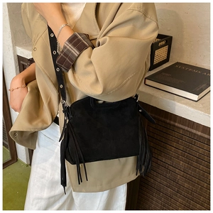 Detail view of black faux-suede crossbody bag featuring long tassels and wide shoulder strap