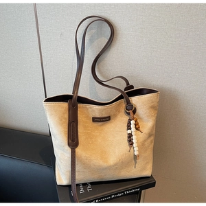 Close-up of beige suede tote bag featuring brown leather handles and wooden bead tassel