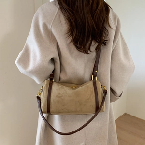 Détail du sac seau en daim kaki avec bandoulière en cuir et finitions dorées sur manteau beige