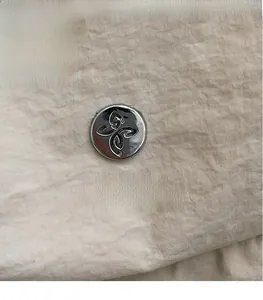 Close-up of beige twill fabric texture with circular brand logo and metal floral emblem