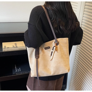 Detail view of beige suede tote bag featuring retro wooden bead charm and brown straps