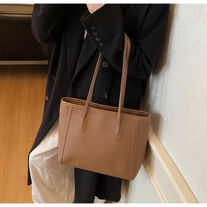 Close-up of brown pebbled leather tote bag with long handles shown on model for size