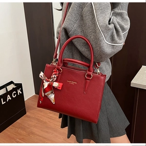 Close-up of red pebbled leather tote with decorative silk scarf and gold brand logo