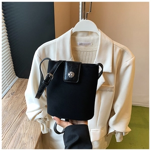 Detail of black bucket bag with leather flap, metal buckle, and adjustable strap